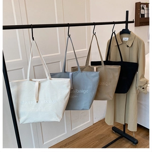 Detailed view of large canvas tote bags in four neutral colors hanging on a metal rack