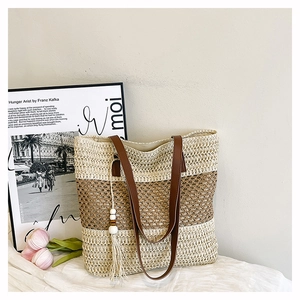 Detail view of a striped straw tote with brown leather straps and beaded tassel charm
