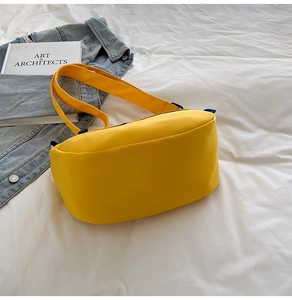 Minimalist bright yellow nylon crescent bag laid on white bedding with a denim jacket