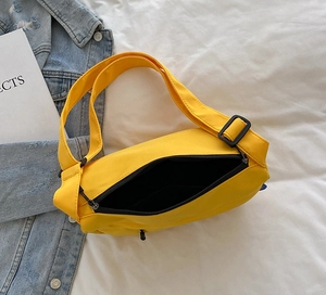 Close-up of bright yellow canvas crossbody bag with black zipper and adjustable buckle