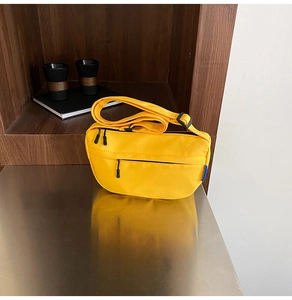 Close-up of vibrant yellow half-moon canvas bag with dual zippers on reflective desk