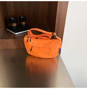 Detail of orange nylon crescent crossbody bag with black zippers on metallic surface