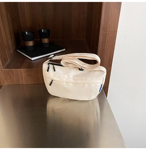 Detail of beige nylon crescent crossbody bag with black dual zipper on metal surface
