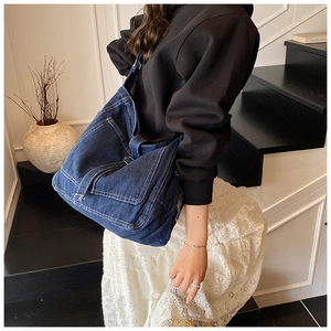 Detail of dark blue washed denim tote bag with white stitching and metal buckle