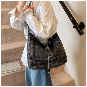 Detail of black vintage washed denim tote bag with frayed edges and silver buckle