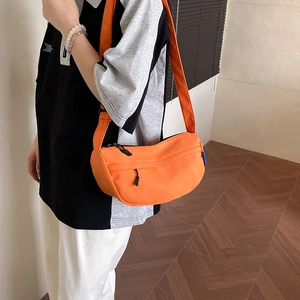 Bright orange crescent nylon crossbody bag with adjustable strap worn by model