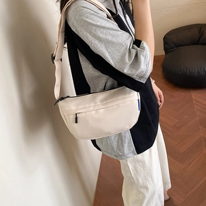 Minimalist beige half-moon crossbody bag with wide black strap and front pocket