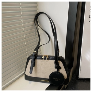 Close-up of beige canvas handbag with black leather trim and elegant gold zippers
