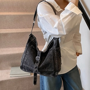 Black denim tote bag with silver buckles and adjustable strap worn by a model