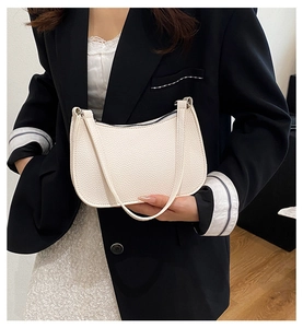 Detail of off-white pebbled leather baguette bag held by a model in a black suit