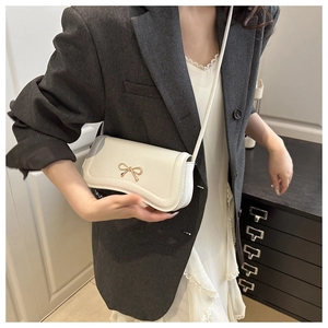 Detailed view of white baguette bag with gold bow clasp on a crossbody strap