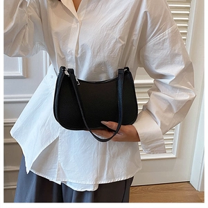 Detail of minimalist black baguette bag with lychee grain texture and silver hardware