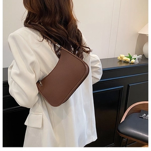 Detail of dark brown lychee textured leather underarm bag on a white blazer