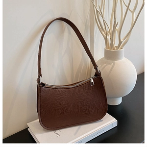Detailed close-up of dark brown lychee textured leather crescent shoulder bag on books