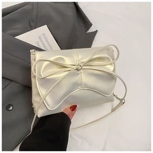 Close-up of cream satin ballet-style handbag with large decorative bow and chain strap