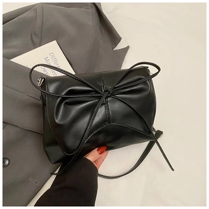 Close-up of black PU leather bag with large bow detail and textured pleats on fabric background