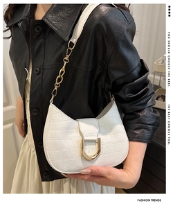 Detail of white crocodile pattern shoulder bag with a large gold horseshoe metal buckle