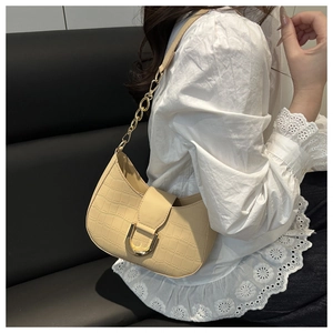 Detail of cream croc-embossed underarm bag with gold U-buckle and chain strap on shoulder