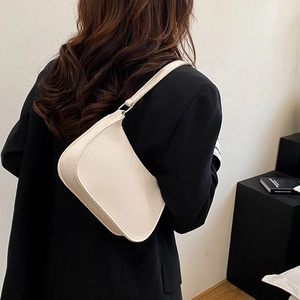 Minimalist beige pebble leather underarm bag worn with a black blazer for chic style