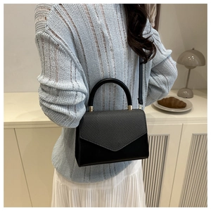 Detail of minimalist black handbag showing woven texture flap and gold hardware accents
