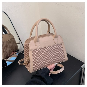 Close-up of herringbone weave texture and faux leather handles on a beige shell bag