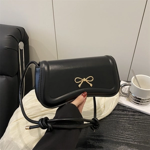 Elegant black crossbody bag with golden bow closure shown in a lifestyle setting