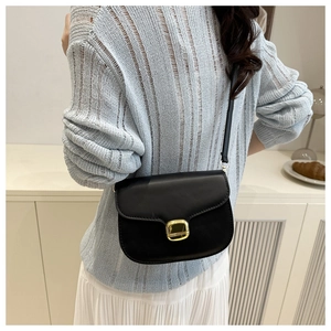Close-up of a vintage black crossbody bag with gold buckle on a stylish model