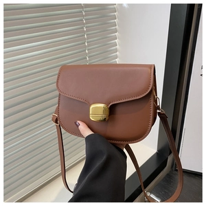 Close-up of caramel leather saddle bag featuring a large rectangular gold metal lock detail