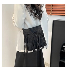Close-up of black fringe shoulder bag with matte suede texture on model in white blazer