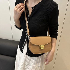 Minimalist camel leather saddle bag with gold buckle worn on shoulder for women