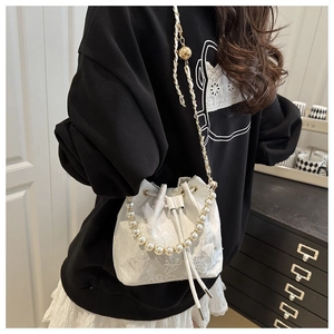 Detail of white floral lace bucket bag featuring pearl handle and chain strap on model
