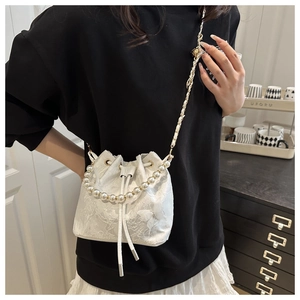 Detailed shot of a white lace bucket bag featuring pearl handles and 3D butterfly accents
