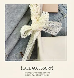 Detail of white leather shoulder bag featuring a large cream lace bow on denim background