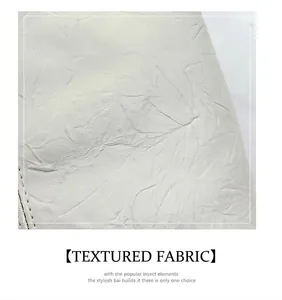 Close-up of white wrinkled leather texture with distinct black stitching on tote bag