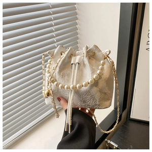 Détail du sac seau en dentelle blanche avec motifs floraux, perles et touches de papillon