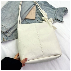 Detailed view of white textured tote bag featuring a decorative lace bow on the shoulder strap