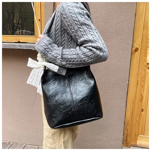 Close-up of black wrinkled leather tote bag with white lace bow charm detail