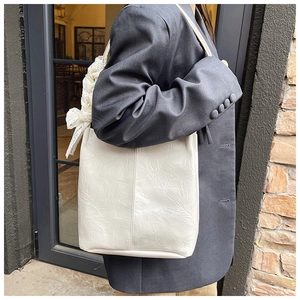 Chic cream tote bag with lace bow detail shown on shoulder with grey blazer