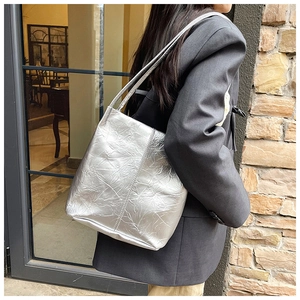 Detailed view of a silver tote bag with metallic pleated texture worn over the shoulder