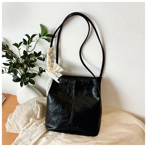 Detail of black faux leather bucket bag with elegant white lace bow charm on wood desk