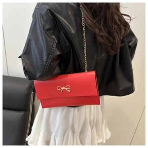 Detail of red leather crossbody bag with golden bow clasp and metal chain strap