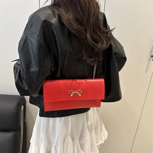 Sac à bandoulière en cuir rouge avec nœud doré et chaîne, porté par un mannequin