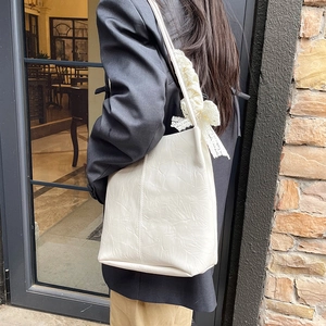 White pleated leather shoulder bag with lace bow accessory shown in an outdoor setting