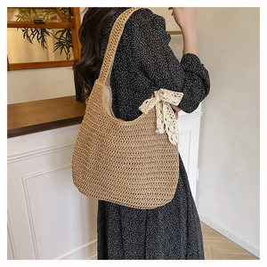 Détail du sac hobo en paille tressée avec un nœud en dentelle crème pour l'été