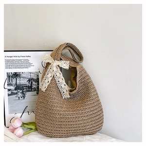 Detail of hand-woven straw tote bag featuring a white lace bow and fabric lining