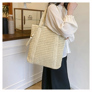 Detail of hollow woven straw tote bag featuring decorative fringe and bead tassel accents