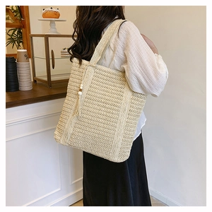Detail of a beige woven straw tote bag with elegant tassels and wooden bead accents