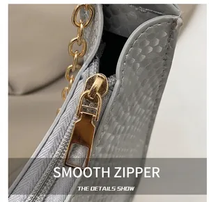 Close-up of smooth gold zipper and grey snakeskin texture on luxury baguette bag