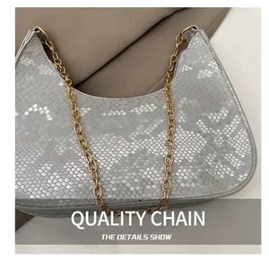 Close-up of snake skin texture and gold chain strap on a silver crescent shoulder bag