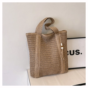 Detail of straw woven tote bag featuring white beaded fringe and boho tassel accents